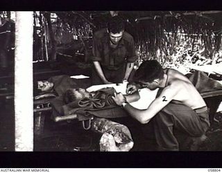 DUMPU, NEW GUINEA. 1943-10-15. VX70603 PRIVATE (PTE) L. CAWTHAN, MEDICAL ORDERLY, ADMINISTERS A NEEDLE OF MORPHINE TO A PATIENT AT THE 2/6TH AUSTRALIAN FIELD AMBULANCE WITH "E" SURGICAL TEAM WHILE ..