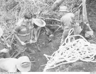 SHAGGY RIDGE, NEW GUINEA. 1943-12-27. AN ENEMY BUNKER ON THE "PIMPLE" CONTAINING THE BODIES OF FOUR JAPANESE BEING FILLED IN BY TROOPS OF THE 2/16TH AUSTRALIAN INFANTRY BATTALION, 21ST AUSTRALIAN ..