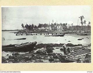 HANSA BAY, NEW GUINEA. 1944-06-22. LOOKING WEST ALONG THE WREAKAGE LITTERED BAY SHORES, SHOWING THE JETTY AND DAMAGED JAPANESE BARGES. IN THE BACKGROUND ARE THE TENTS OF THE 5TH DIVISION SALVAGE ..