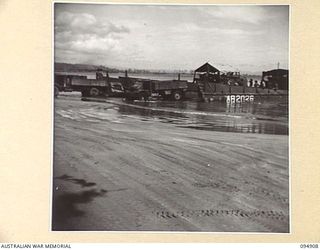 BORAM BEACH, NEW GUINEA. 1945-08-06. TRUCKS OF HEADQUARTERS COMMAND, AUSTRALIAN ARMY SERVICE CORPS 6 DIVISION, BEING LOADED FROM AUSTRALIAN LANDING CRAFT WHICH HAVE BROUGHT SUPPLIES ASHORE FROM AN ..