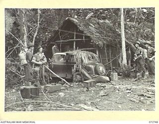 MADANG, NEW GUINEA. 1944-04-26. MEMBERS OF THE 57/60TH INFANTRY BATTALION BESIDE AN ABANDONED JAPANESE STAFF CAR OUTSIDE NATIVE HUTS ON BOARD THE BOGADJIM ROAD NEAR BOGADJIM. THE HUTS WERE USED AS ..