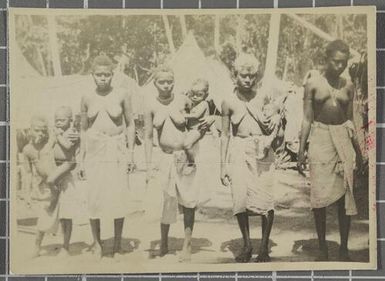 Four women and four children outside huts in the village of Nissan