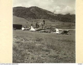 The top portion of the Wau airstrip which is unique in that it runs up the slope of a hill requiring pilots to use judgment in landing. The aircraft are, from left to right, a CAC Wirraway of 4 ..