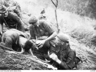 THE 2/3RD AUSTRALIAN INDEPENDENT COMPANY AT "TIMBERED KNOLL" NORTH OF ORODUBI, NEW GUINEA, ON 1943-07-29. CORPORAL R. R. S. GOOD ABOUT TO DRESS THE WOUNDS OF PRIVATE H. W. ROBINS WITH THE ..