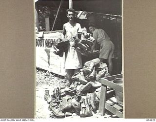 1943-04-12. NEW GUINEA. CPL. F. CARDINER OF SOUTH YARRA, MELBOURNE WITH BOOTS OF AN ALLIED UNIT WHICH WERE LEFT AT THIS BOOT REPAIRING DEPOT IN NEW GUINEA HUNDRED OF PAIRS ARE REPAIRED WEEKLY FOR ..
