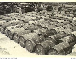 MILNE BAY, NEW GUINEA. 1944-04-04. NATIVE LABOURERS LOAD 44 GALLON DRUMS OF 80 OCTANE MOTOR SPIRIT AT THE 2ND AUSTRALIAN BULK PETROLEUM STORAGE COMPANY FOR SUPPLY TO UNIT DUMPS AND SHIPMENT TO ..