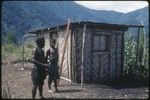 Small tin-roofed tradestore, Wando and another man