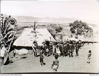 Garoka, New Guinea, 1945. Dressed in ceremonial costume, a group of native Papuans performs a traditional dance and 'sing-sing' in their village. The man at centre is carrying a large cult or totem ..