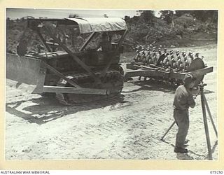 PALMALMAL PLANTATION, NEW BRITAIN. 1945-02-14. A TRACTOR AND SHEEPSFOOT ROLLER MOVING PAST A SURVEYOR DURING THE BUILDING OF THE NEW AIRSTRIP BY PERSONNEL OF THE 2/3RD RAILWAY CONSTRUCTION COMPANY. ..