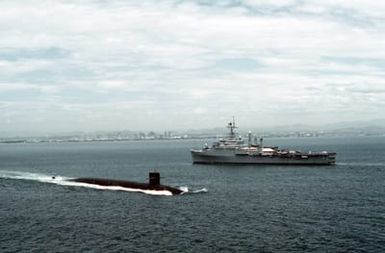 An Ohio class submarine travels out to sea as the miscellaneous flagship USS CORONADO (AGF-11) approaches Naval Air Station, North Island, San Diego. The CORONADO, flagship for Commander, Third Fleet, will be arriving at its new home port after being stationed in Hawaii for almost 20 years