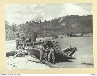 KAMANDRAN JETTY, NEW BRITAIN. 1945-02-17. PERSONNEL OF THE 5TH SURVEY BATTERY EXAMINING ONE OF THE SEVEN WRECKED JAPANESE BARGES AT THE JETTY. NOTE THE APTLY NAMED SCARFACE HILL IN THE BACKGROUND. ..