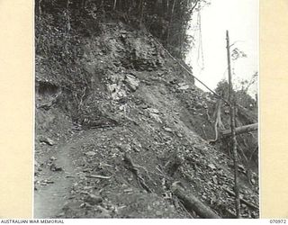 ZENAG, NEW GUINEA, 1944-02-28. IN ORDER TO WIDEN THE EXISTING TRACK, THE ROCK FACE HAS BEEN BLASTED, BRINGING DOWN EARTH WHICH WILL BE CLEARED BY BULLDOZERS