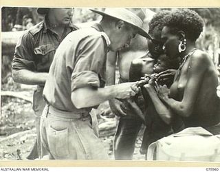 BOUGAINVILLE, PURIATA RIVER. 23RD MARCH, 1945. NX72249 CAPTAIN G.M. BRODIE, 11TH FIELD AMBULANCE, AUSTRALIAN ARMY MEDICAL CORPS (1), IMMUNISING A PICCANINNY, (HELD BY MOTHER), AGAINST YAWS. THE ..