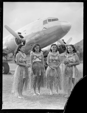 Four unidentified young island girls in costume, in front of a C47 aircraft, Rarotonga, Cook Islands