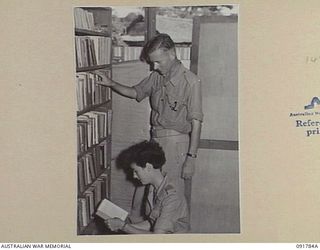 LAE, NEW GUINEA. 1945-05-15. PRIVATE E.H. FINLAYSON (1), ASSISTS PRIVATE G.H. BRENNAND (2), TO SELECT A BOOK FROM THE ARMY EDUCATION SERVICE LIBRARY. PRIVATE FINLAYSON IS ONE OF A GROUP OF ..