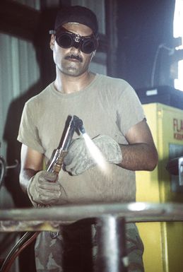 Steelworker Second Class (SW2) Frank Luevanos prepares to cut a piece of sheet metal in the welding shop of the Naval Mobil Construction Battalion Three (NMCB-3) Civic Action Team compound