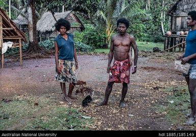 Group with piglet and puppies. Girl with piglet tethered on string in Kauwai. Bosko on right