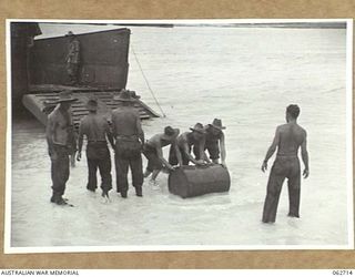 SIALUM, NEW GUINEA. 1944-01-05. PERSONNEL OF "D" COMPANY, 2/3RD AUSTRALIAN PIONEER BATTALION UNLOADING 44 GALLON DRUMS OF PETROL FROM AN LCM (LANDING CRAFT, MECHANISED) ON TO THE BEACH