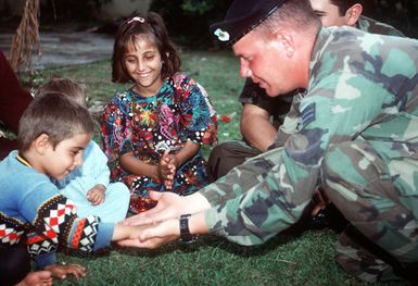 SRA Eric Ruiter, a security policeman from Hickam Air Force Base, Hawaii demonstrates a little American culture for Kurdish children with some "low fives." The children, airlifted from Turkey, were part of Operation Pacific Haven, a U.S. State Department-directed action aimed at evacuating Kurds and other Iraqi opposition groups from the Middle East country's turmoil. Exact Date Shot Unknown Published in AIRMAN Magazine June 1977