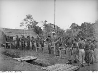 KIARIVU, NEW GUINEA, 1945-08-14. WARRANT OFFICER 2 T. HEALEY, THE AUSTRALIAN NEW GUINEA ADMINISTRATIVE UNIT REPRESENTATIVE IN KIARIVU RAISES THE UNION JACK OUTSIDE KIAP HOUSE, THE GOVERNMENT ..