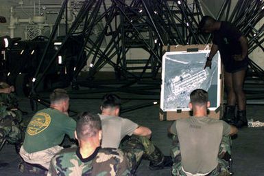 US Marine Sergeant Mark J. Palmer (In black shorts and T-shirt), Jumpmaster, 3rd Air Delivery Platoon, Landing Support Company, 3rd Support Battalion, 3rd Force Service Support Group, briefs Marines, 2nd Platoon, Company A, 5th Force Reconnaissance Battalion, 3rd Marine Division, on the drop zones before they jump from a US Air Force C-141 Starlifter (Not shown) aircraft during the Force Reconnaissance Exercises