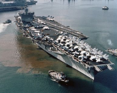 A starboard bow view of the nuclear-powered aircraft carrier USS ENTERPRISE (CVN 65) in Pearl Harbor. Several large tugs are maneuvering around the carrier