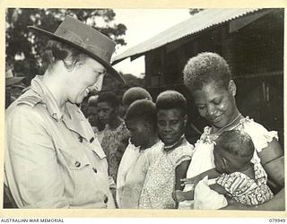 LAE, NEW GUINEA. 1945-03-27. LADY WAKEHURST, TALKS TO A NATIVE CHILD IN THE ARMS OF ITS MOTHER DURING A VISIT TO THE FAMILIES OF MEMBERS OF THE ROYAL PAPUAN CONSTABLULARY