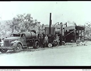 WARDS STRIP, PORT MORESBY, NEW GUINEA, 1943-03. A BITUMEN SPRAYER BEING FILLED WITH HOT MIX BITUMEN BY MEMBERS OF THE RAAF. MACHINERY AND BUILDINGS OF THE PLANT AND EMPTY BARRELS CAN BE SEEN. WARDS ..