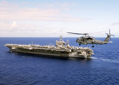 Portside view of the US Navy (USN) Nimitz Class Aircraft Carrier USS CARL VINSON (CVN 70) departing Naval Station (NS) Marianas, Guam (GU), after a four-day port visit. An SH-60 Seahawk helicopter is flying off the port stern of the ship