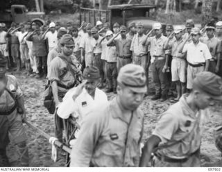 KAHILI, BOUGAINVILLE. 1945-10-01. LIEUTENANT GENERAL H. HYAKUTAKE, A FORMER COMMANDER OF 17 JAPANESE ARMY, IS SALUTED BY TROOPS AS HE IS CARRIED ON A CHAIR TO A LANDING BARGE FOR TRANSPORTATION TO ..