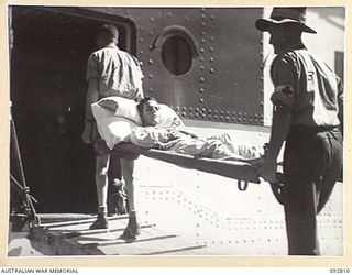 LAE, NEW GUINEA. 1945-06-09. A PATIENT FROM 2/7 GENERAL HOSPITAL BEING CARRIED FROM AN AMBULANCE ON TO THE HOSPITAL SHIP MANUNDA AT MILFORD HAVEN WHARF