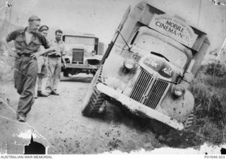 PORT MORESBY, PAPUA, 1942. THE FORD TRUCK "BENNIE", MOBILE CINEMA NO. 76, AUSTRALIAN ARMY AMENITIES SERVICE, WHICH HAS RUN OFF THE ROAD FROM MURRAY BARRACKS. LEFT TO RIGHT: SERGEANT GEOFF MASTERS, ..