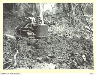 GUY'S POST - MAIN STREAM ROAD, DUMPU AREA, NEW GUINEA. 1944-04-16. VX135637 SAPPER J. BENSON, 15TH FIELD COMPANY, ROYAL AUSTRALIAN ENGINEERS TRIMMING THE ROAD WITH A BULLDOZER DURING CONSTRUCTION