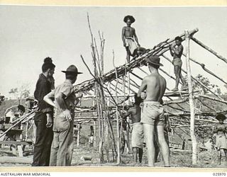 PORT MORESBY, PAPUA. 1942-07-20. AMERICAN SOLDIERS WATCHING PAPUAN NATIVES ERECTING GRASS AND WOOD HUTS WHICH WILL BE OCCUPIED BY AMERICAN TROOPS