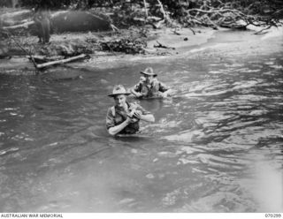 WEBER'S CREEK, NEW GUINEA, 1944-02-09. VX7208 SERGEANT F. MCKECHNIE (1) OF THE MILITARY HISTORY SECTION, NEW GUINEA FORCE, HOLDS HIS CAMERA HIGH AS HE CROSSES WEBER'S CREEK WITH MR JOHN QUINN (2), ..