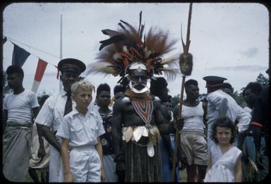 Highland native wearing bird of paradise plumes at Wabag, government appointed headmen wearing red banded caps in the background, between 1955 and 1960 / Tom Meigan