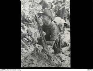 Finisterre Range, New Guinea. 23 March 1944. Private P. H. Simpson of Rose Park, SA, is all mud and a big grin in the last stages of a 3000 ft climb to "Kingsley's Downfall" in this tough ..