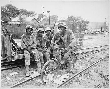 "Negro Marines, attached to the Third Ammunition Company, take time out from supplying ammunition to the front line on Saipan. Riding captured...bicycle is Pfc. Horace Boykin; and left to right, Cpl. Willis T. Anthony, Pfc. Emmitt Shackelford, and Pfc. Eugene Purdy."