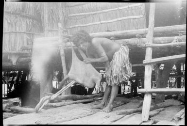 Woman in a house bending over a baby in a net bag, New Guinea, ca. 1929 / Sarah Chinnery