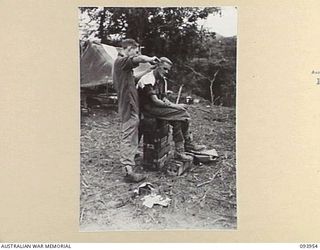 ULUPU, NEW GUINEA, 1945-07-09. PRIVATE I.J. ROBINSON (1), GIVING A HAIRCUT TO PRIVATE E.O. GARTLAN (2), WHO IS SEATED ON AMMUNITION BOXES. THE MEN, MEMBERS OF 16 PLATOON, D COMPANY, 2/5 INFANTRY ..