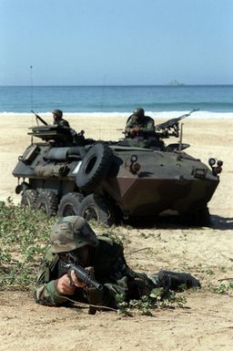 US Marine Corps PFC Martin Vazquez, a member of 1ST Light Armored Reconnaissance, Camp Pendleton, California, help secure the perimeter for an amphibious assault during exercise RIMPAC '98. Behind him are other members of his unit in an armored reconnaissance vehicle and off in the horizon sits a Navy warship