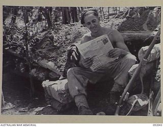 BOUGAINVILLE, 1945-05-16. PRIVATE W.T. KINNANE, D COMPANY, 24 INFANTRY BATTALION READING THE NEWS OUTSIDE HIS FOXHOLE IN A POSITION SOUTH OF THE HONGORAI RIVER