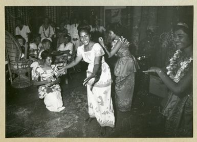 The picture depicts four women performing a dance. In the background, uniform-dressed men are seen as spectators. The picture is taken in Samoa in connection with the mine ship Älvsnabens long voyage 1966-1967.