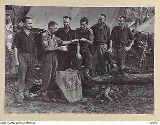 KARAWOP, NEW GUINEA. 1945-05-05. SERGEANT J.C. MINTY, THE POSTAL SERGEANT (2), DISTRIBUTING MAIL TO 2/1 INFANTRY BATTALION TROOPS. IDENTIFIED PERSONNEL ARE:- SERGEANT S.W. HILLS (1); PRIVATE L.J. ..