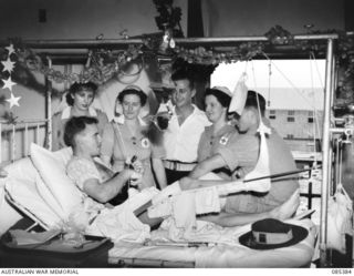 GREENSLOPES, QUEENSLAND. 1944-12-25. DRIVER D. DIXON, MEDICAL STORES, NEW GUINEA FORCE, (1), ALTHOUGH HEAVILY BANDAGED, ENTERTAINS PATIENTS AND MEMBERS OF THE STAFF AT 112 (BRISBANE) MILITARY ..