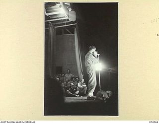 LAE, NEW GUINEA. 1944-07-24. SERGEANT HORRIE DARGIE, AUSTRALIAN MILITARY FORCES, THE AUSTRALIAN HARMONICA EXPERT, RENDERING AN ITEM DURING A CONCERT STAGED FOR THE TROOPS BY THE AMERICAN ..