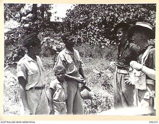 RABAUL, NEW BRITAIN, 1945-09-10. PRIVATE B. LYNCH (1) AND PRIVATE H.E. FIELD (2), MEMBERS OF THE AUSTRALIAN OCCUPATION FORCE, TALKING TO MR ALEX SMITH, HIS SON AND HIS NEPHEW, WHO HAVE BEEN INDIAN ..