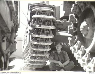 MADANG, NEW GUINEA. 1944-08-23. QX23297 TROOPER T. M. PITKIN RELAXING IN THE SHADE OF A CHURCHILL TANK IV ON THE WHARF. THIS TANK IS ONE OF A CONSIGNMENT OF 32 BROUGHT TO THE AREA BY THE AMERICAN ..