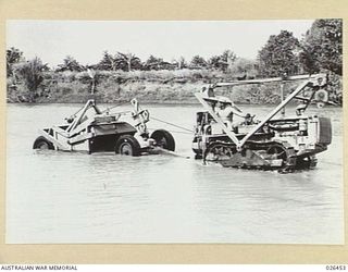 PAPUA, NEW GUINEA. 1942-08. AMERICAN ARMY ENGINEERS ADOPT A NOVEL METHOD FOR OBTAINING GRAVEL FOR SURFACING AN AIRFIELD. A GIANT "GRABALL" IS TOWED INTO THE LOLOKI RIVER AND ENOUGH GRAVEL SCOOPED ..