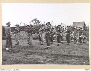 DALLMAN HARBOUR, NEW GUINEA. 1945-11-11. MEMBERS OF THE PIPE BAND, 2/5 INFANTRY BATTALION, PLAYING "FLOWERS OF THE FORREST" DURING A MEMORIAL SERVICE HELD IN THE UNIT LINES IN HONOUR OF THOSE WHO ..